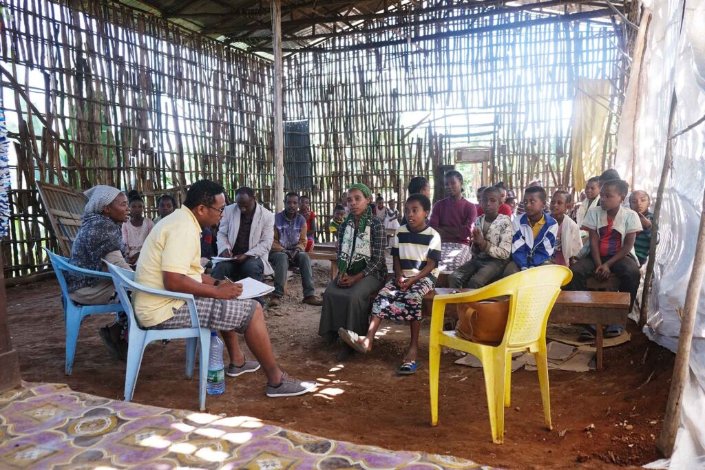social worker talks with a mother and son, seated in the front row of a room filled with adults and children.