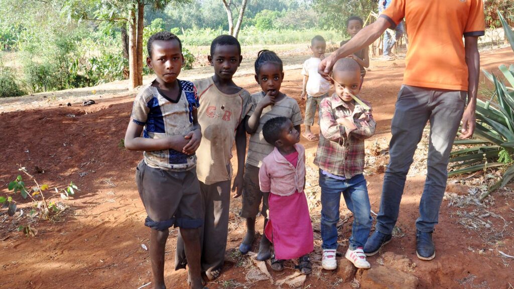 children standing on a dirt road looking shyly at the camera
