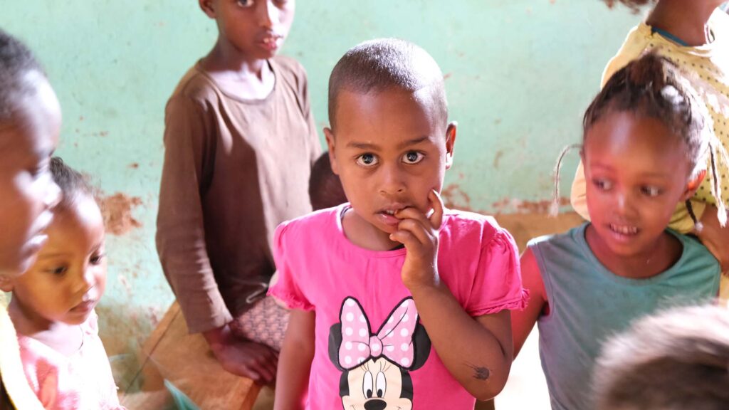little girl wearing pink a Minnie Mouse t-shirt biting her nails while looking shyly at the camera