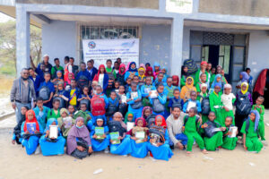 a few dozen children sitting in front of an Ethiopian school with school supplies