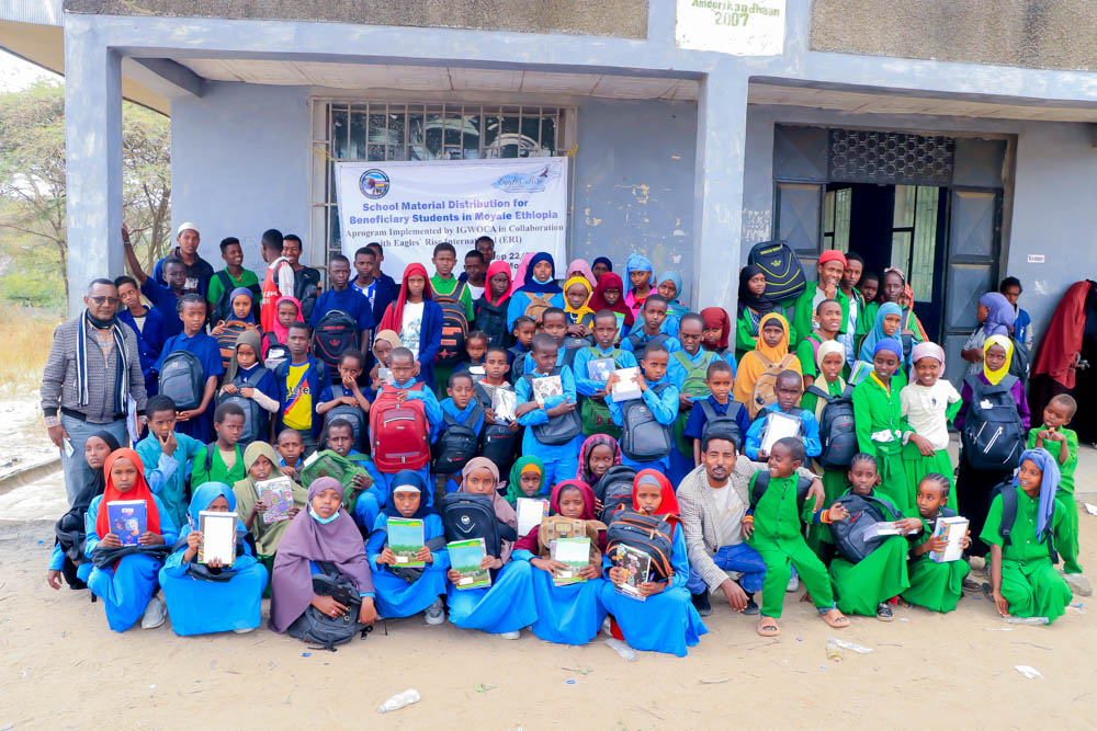a few dozen children sitting in front of an Ethiopian school with school supplies